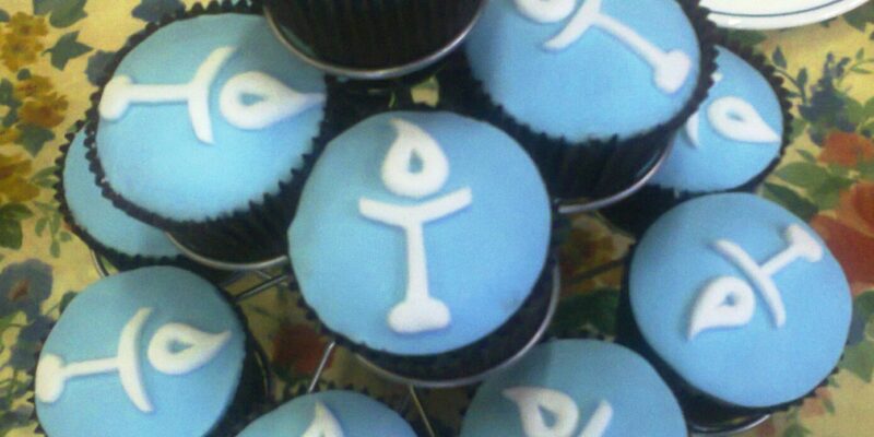 A plate of cupcakes with blue icing and the Unitarian chalice logo on top in white icing.