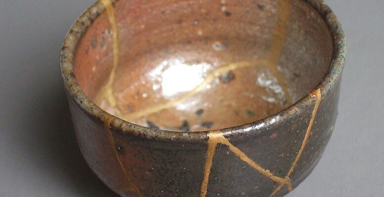A small brown and black bowl mended with the Kintsugi technique of mending cracks with gold.