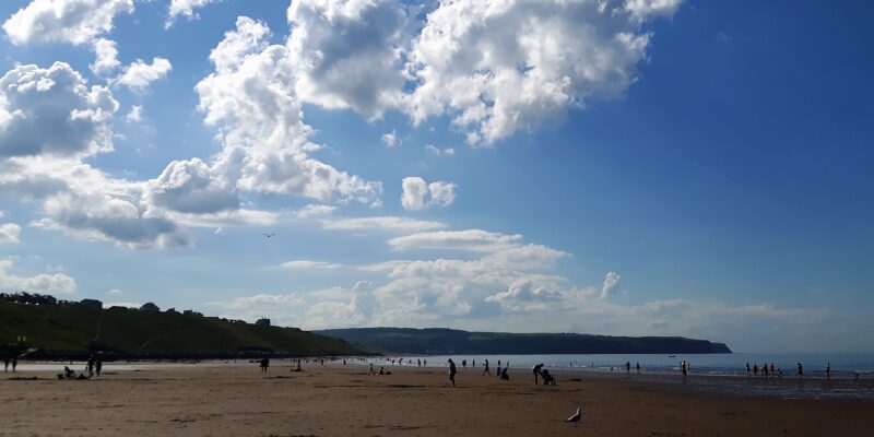Whitby beach in summer, with a blue sky and clouds over the beach.